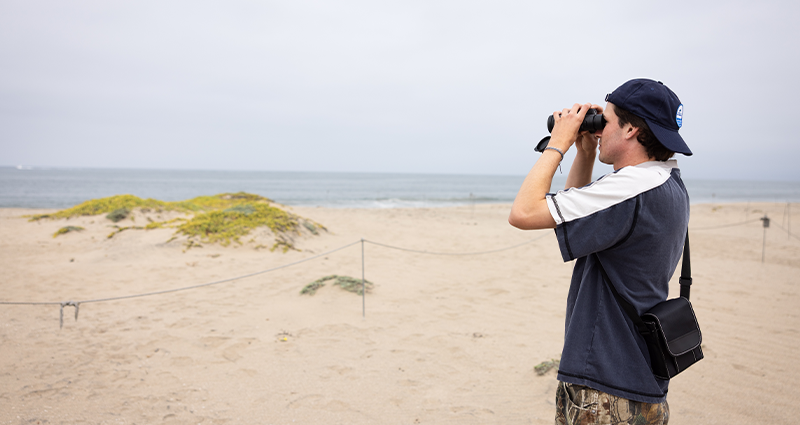LMU student using binoculars for field research at sand dunes